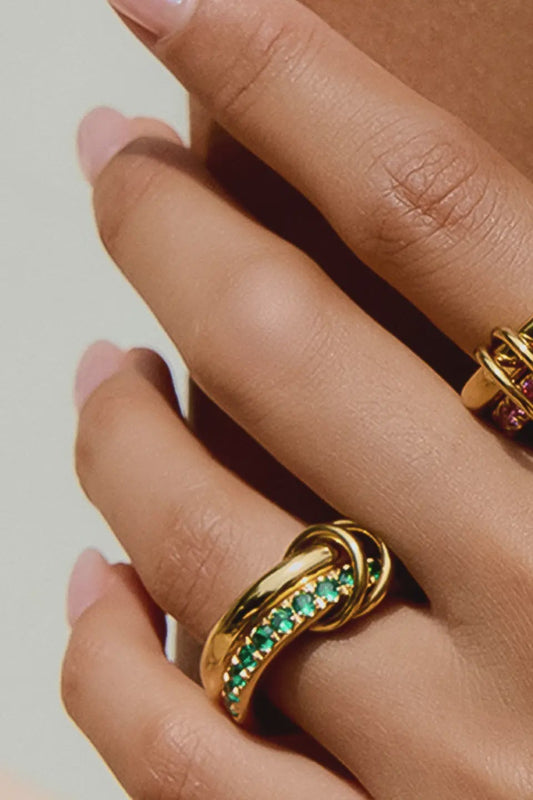 Close-up of a hand wearing two gold rings with gemstones on a neutral background