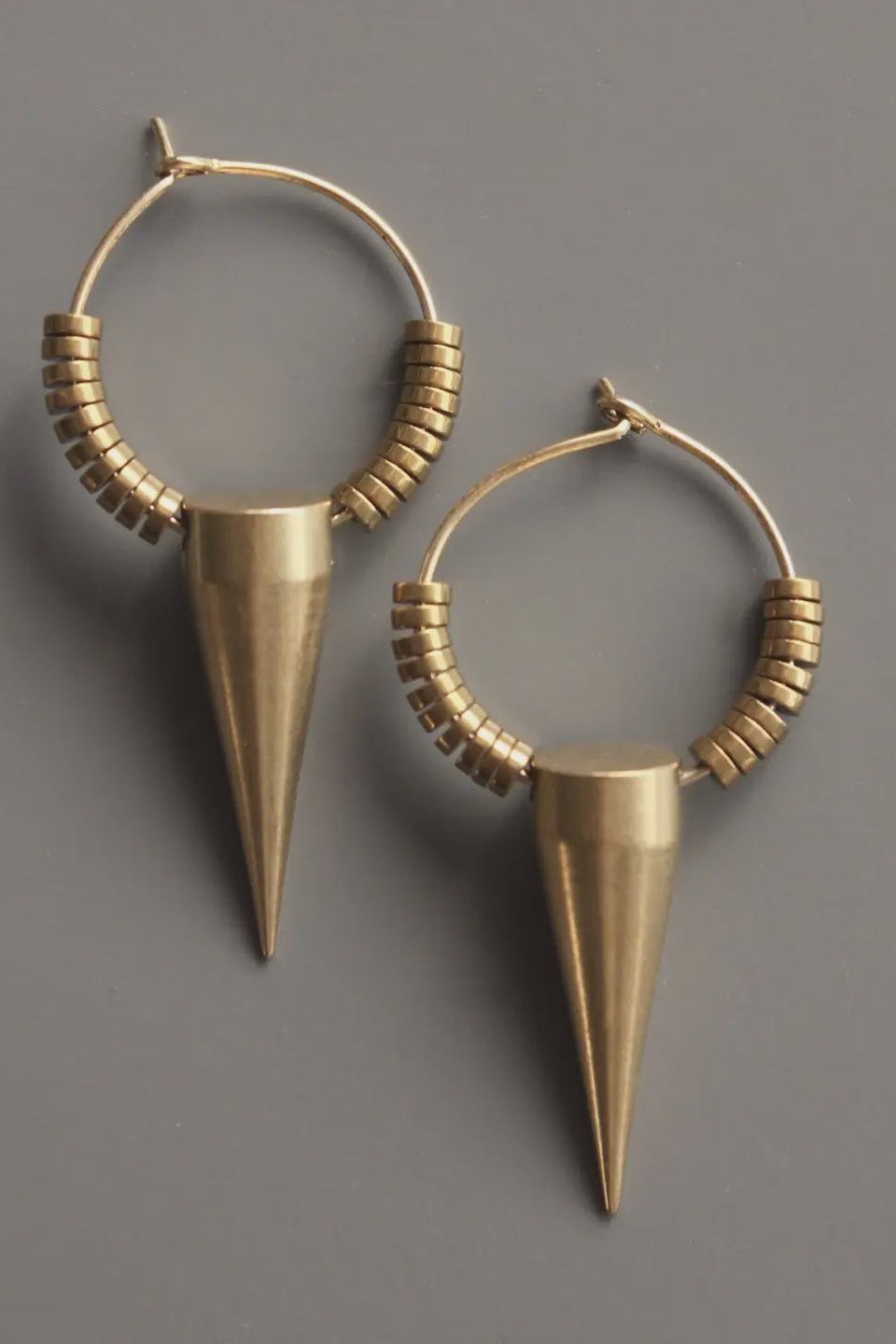Pair of gold hoop earrings with cone-shaped drops on a gray background