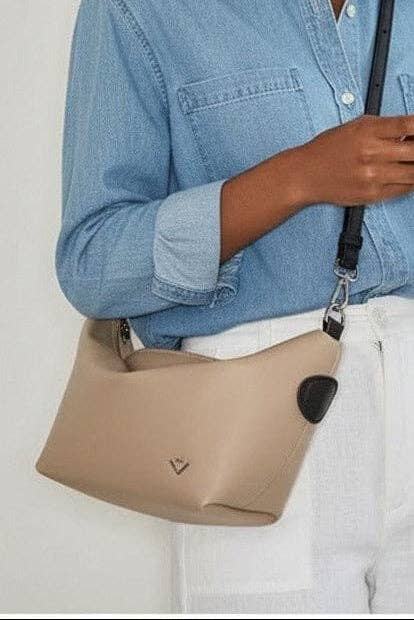 Beige handbag worn by a person wearing a blue denim shirt and white pants on a light gray background