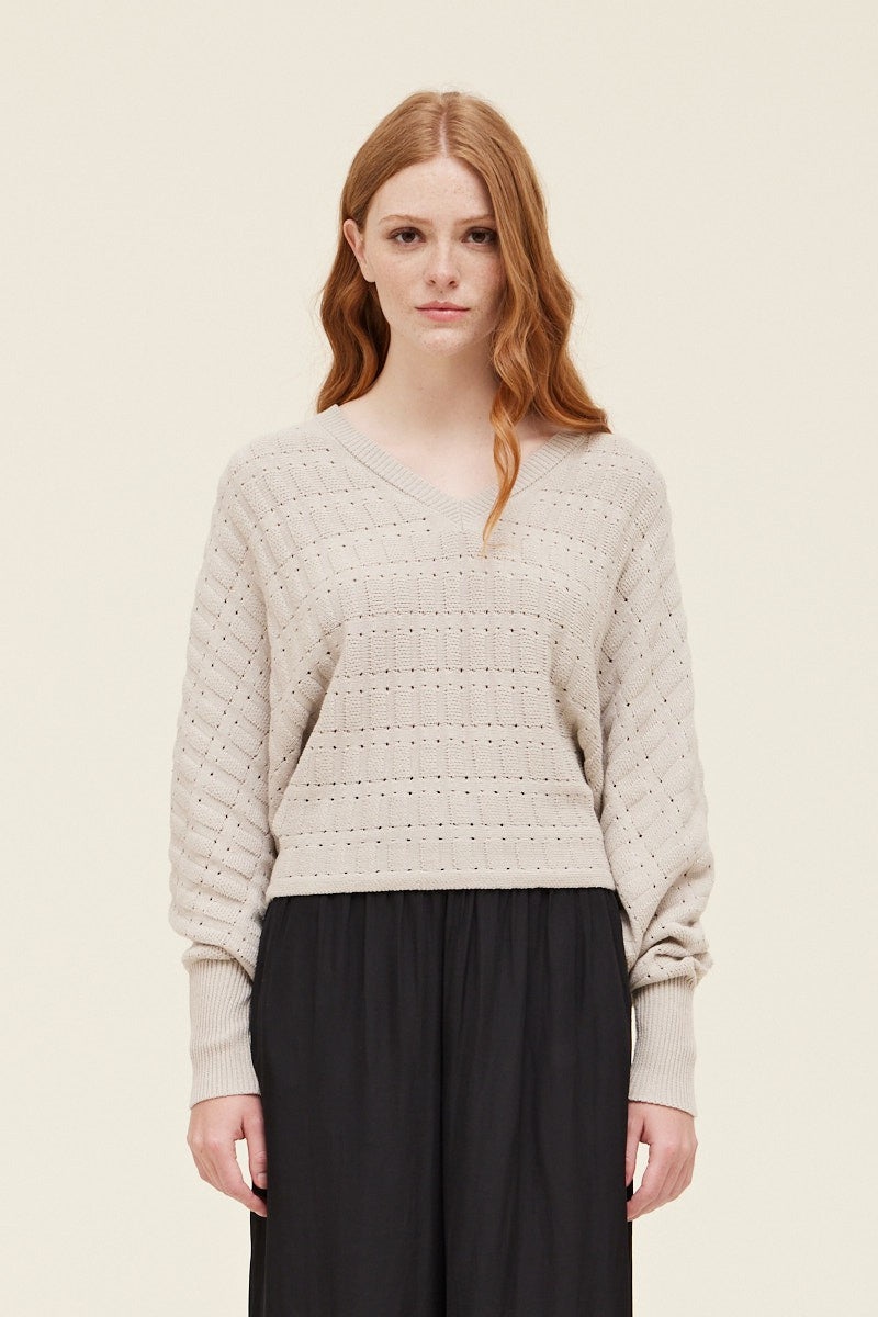 Woman wearing a light beige knitted sweater and black pants on a plain background