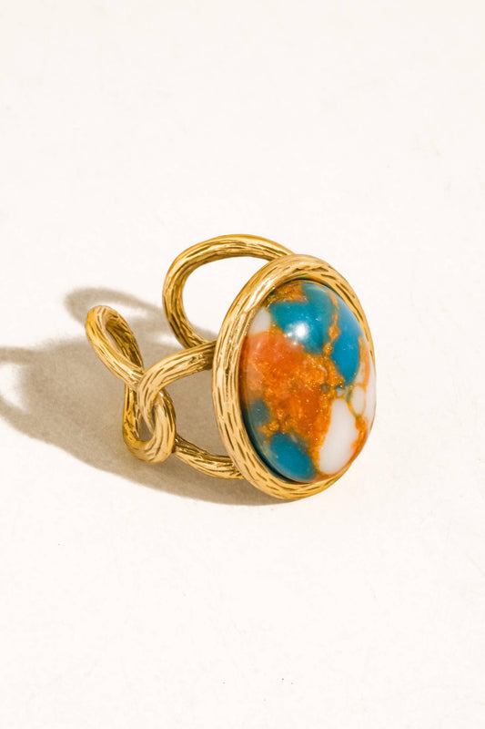 A gold ring with a twisted wrap design and a large oval cabochon featuring a marbled pattern of turquoise blue, orange, and white, set against a plain white background.