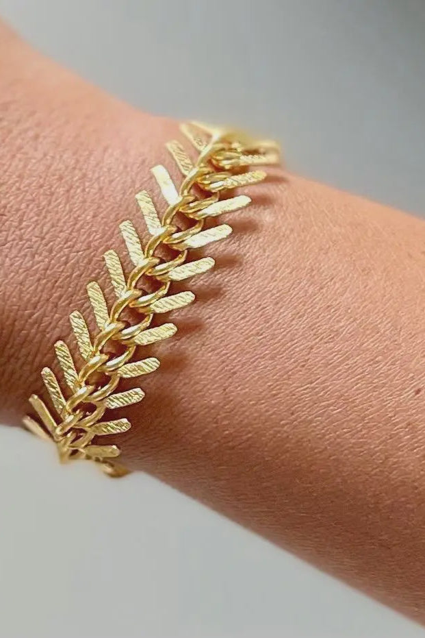Gold bracelet on a wrist with a neutral background