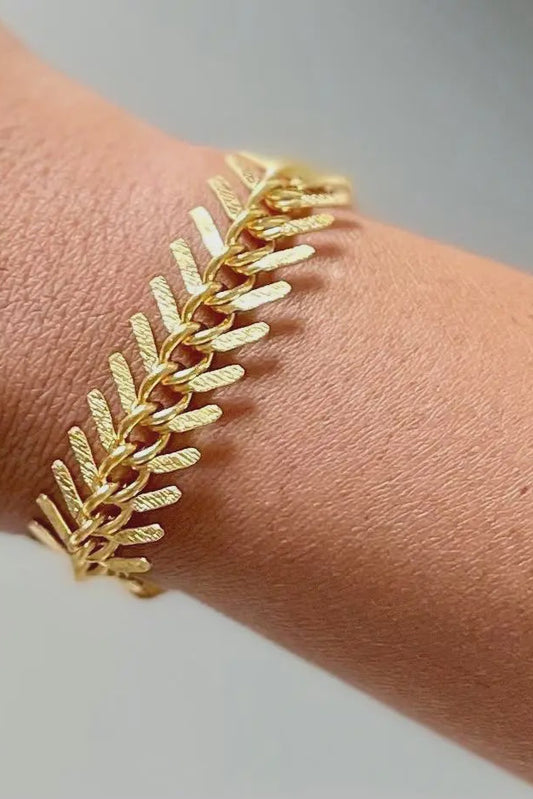 Gold bracelet on a wrist with a neutral background