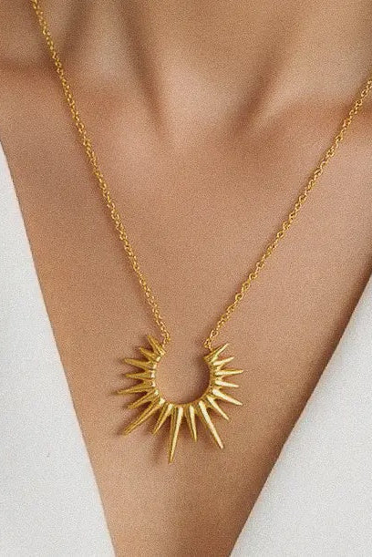 Gold necklace with a sunburst pendant on a person wearing a white outfit.