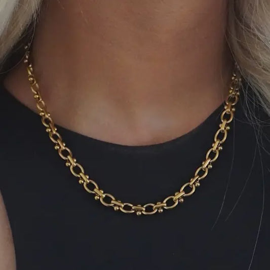 Gold chain necklace worn by a person on a black background