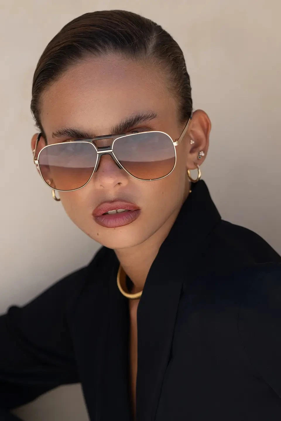 Person wearing gold aviator sunglasses and a black outfit against a neutral background