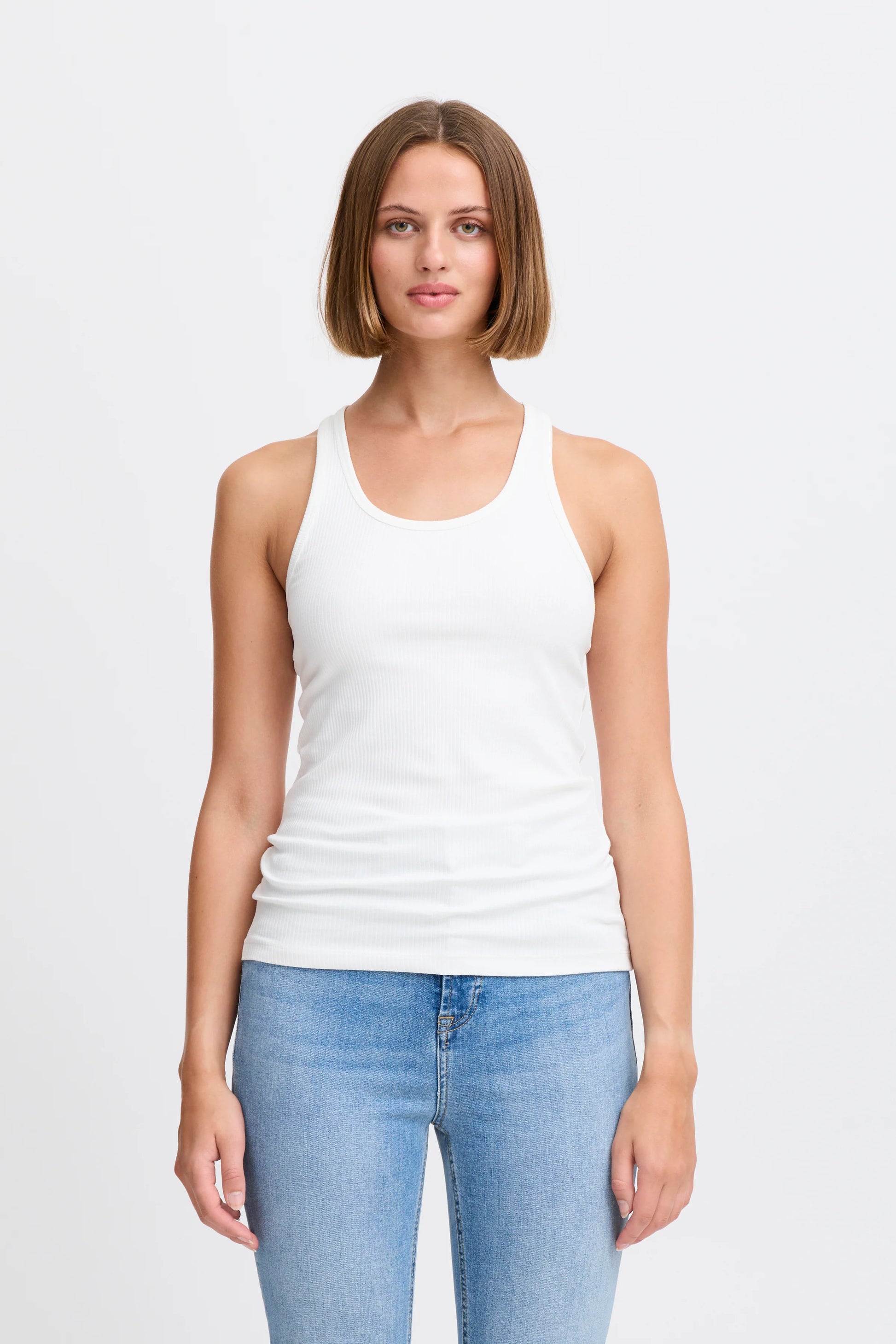 Woman wearing a white tank top and blue jeans on a plain background
