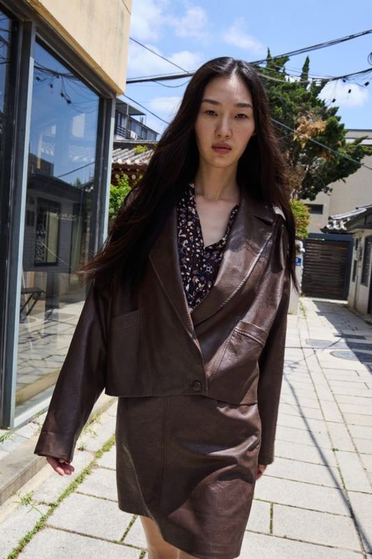 Woman in a brown suit standing on a street with buildings and trees in the background