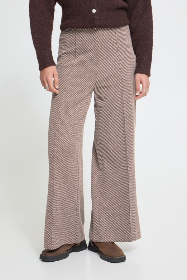 Person wearing brown checkered pants and a brown sweater on a white background