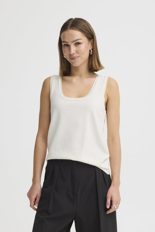 Woman wearing a white sleeveless top and black pants on a plain background