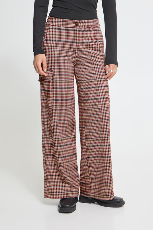 A person wearing high-waisted, wide-leg trousers with a red, black, and beige plaid pattern, styled with a black long-sleeve top and black shoes against a light gray studio background.