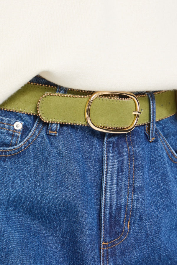 An olive green belt with a gold-tone oval buckle, shown worn over blue denim jeans against a plain off-white background.