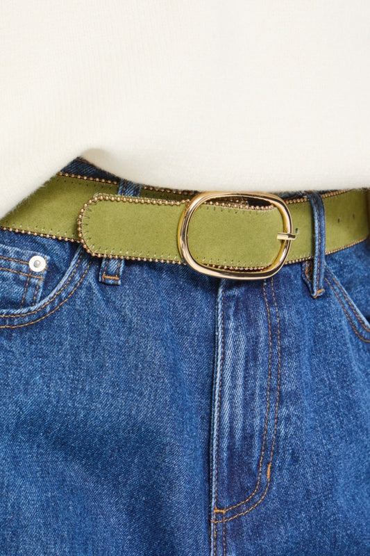 An olive green belt with a gold-tone oval buckle, shown worn over blue denim jeans against a plain off-white background.