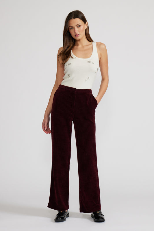 Woman wearing a white tank top and burgundy pants on a white background