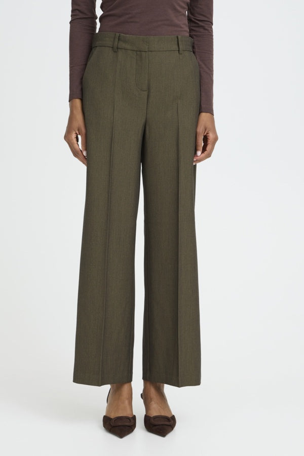 A model is wearing a pair of olive green wide-leg cropped trousers with a subtle vertical stripe texture, paired with a dark brown long-sleeve top and dark brown pointed-toe flats, against a plain white studio background.