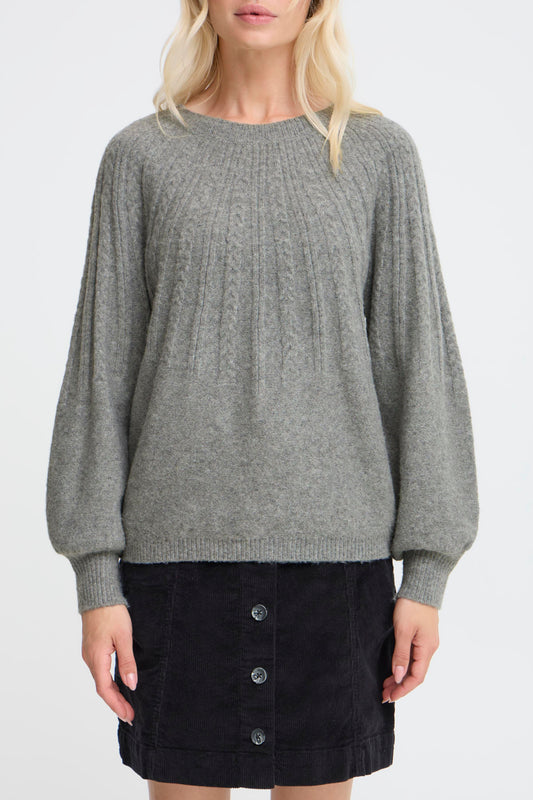 Woman wearing a gray sweater over a black skirt on a white background