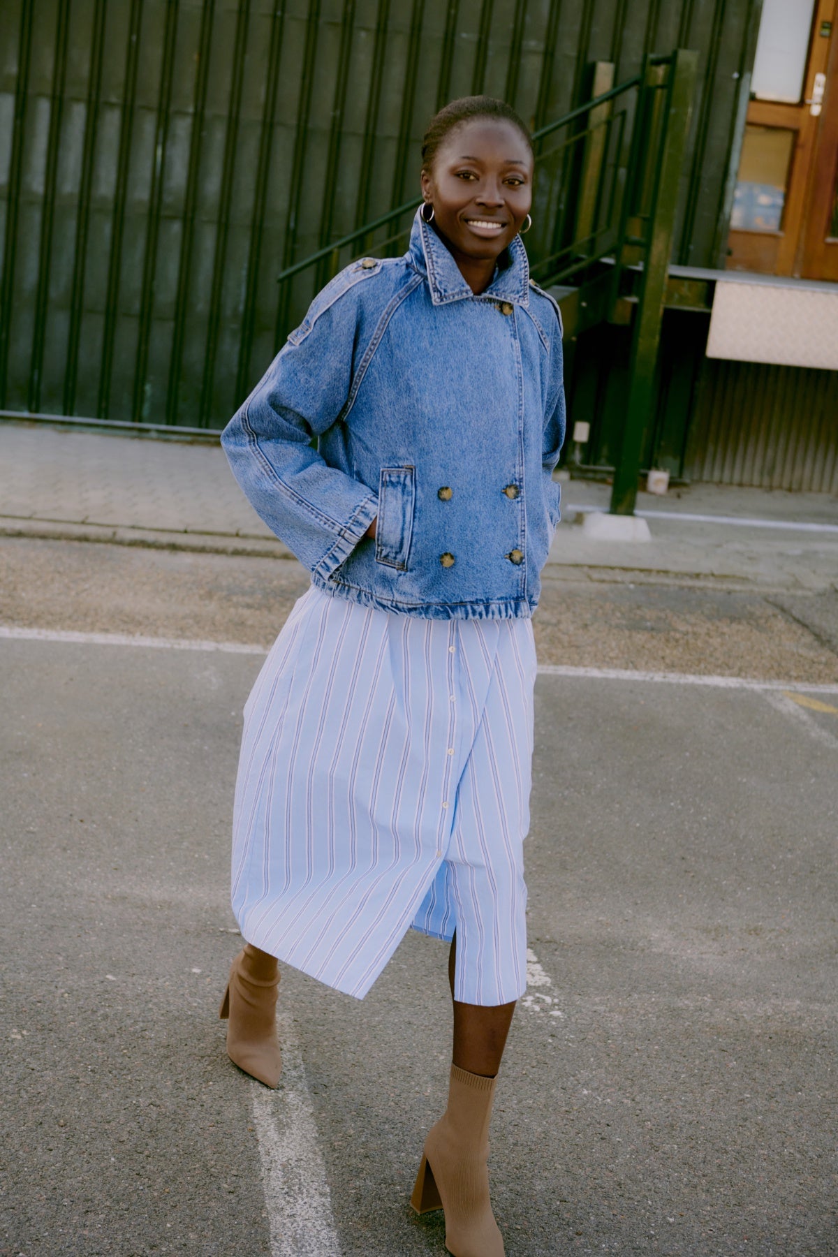 Woman wearing a denim jacket and light blue dress standing on a street.