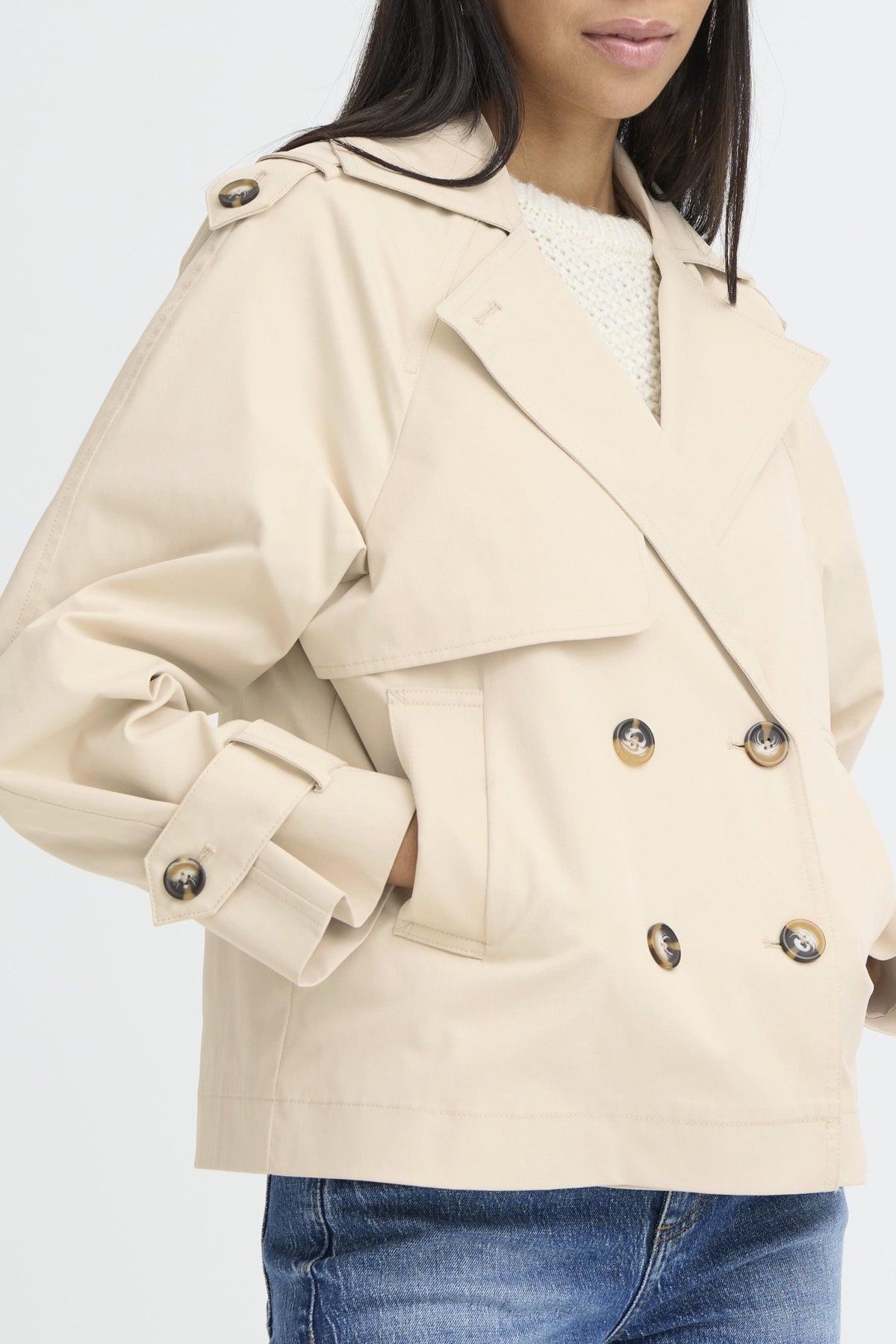 Beige trench coat with gold buttons worn by a person on a white background