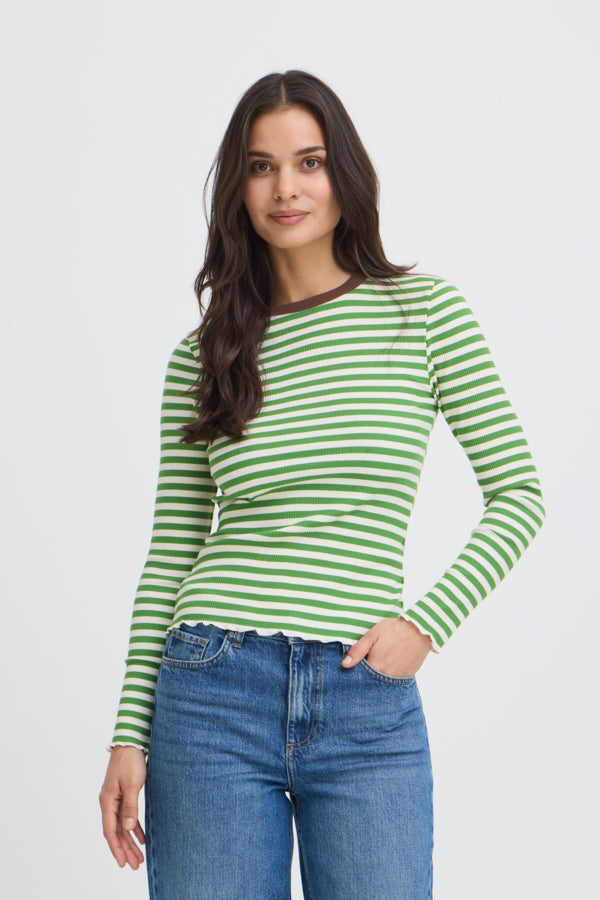 A woman modeling a green and white striped long-sleeve top with a dark brown crew neck, paired with blue jeans, against a light gray studio background.