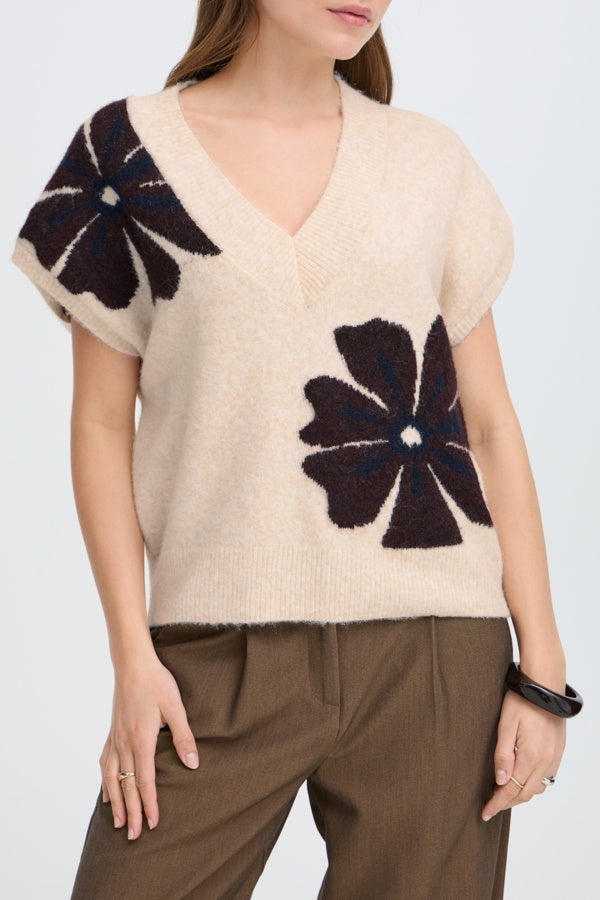 Beige sweater with brown floral patterns worn by a person on a white background