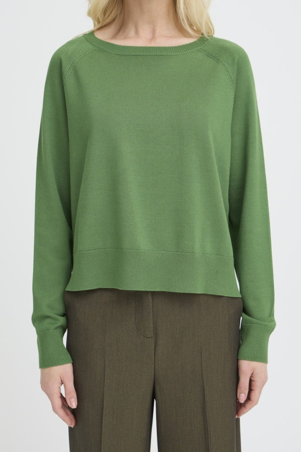 Person wearing a green sweater and brown pants on a white background