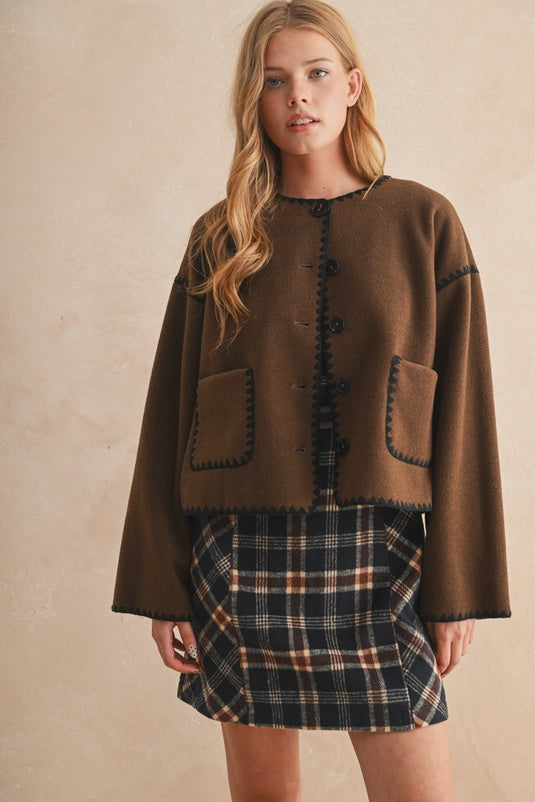 Woman wearing a brown jacket and plaid skirt against a beige background