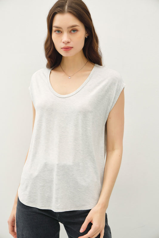 A woman wearing a light gray sleeveless scoop-neck t-shirt and dark gray jeans, standing against a plain light gray background.