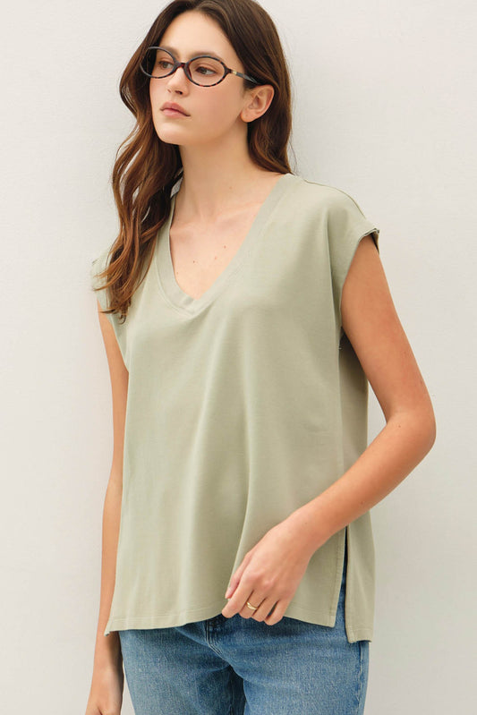 Woman wearing a light green sleeveless top and blue jeans against a plain background