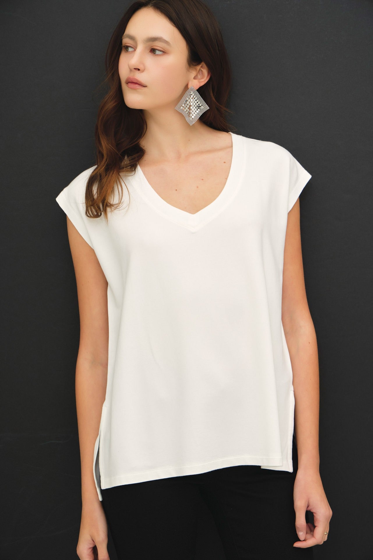 Woman wearing a white sleeveless top against a black background