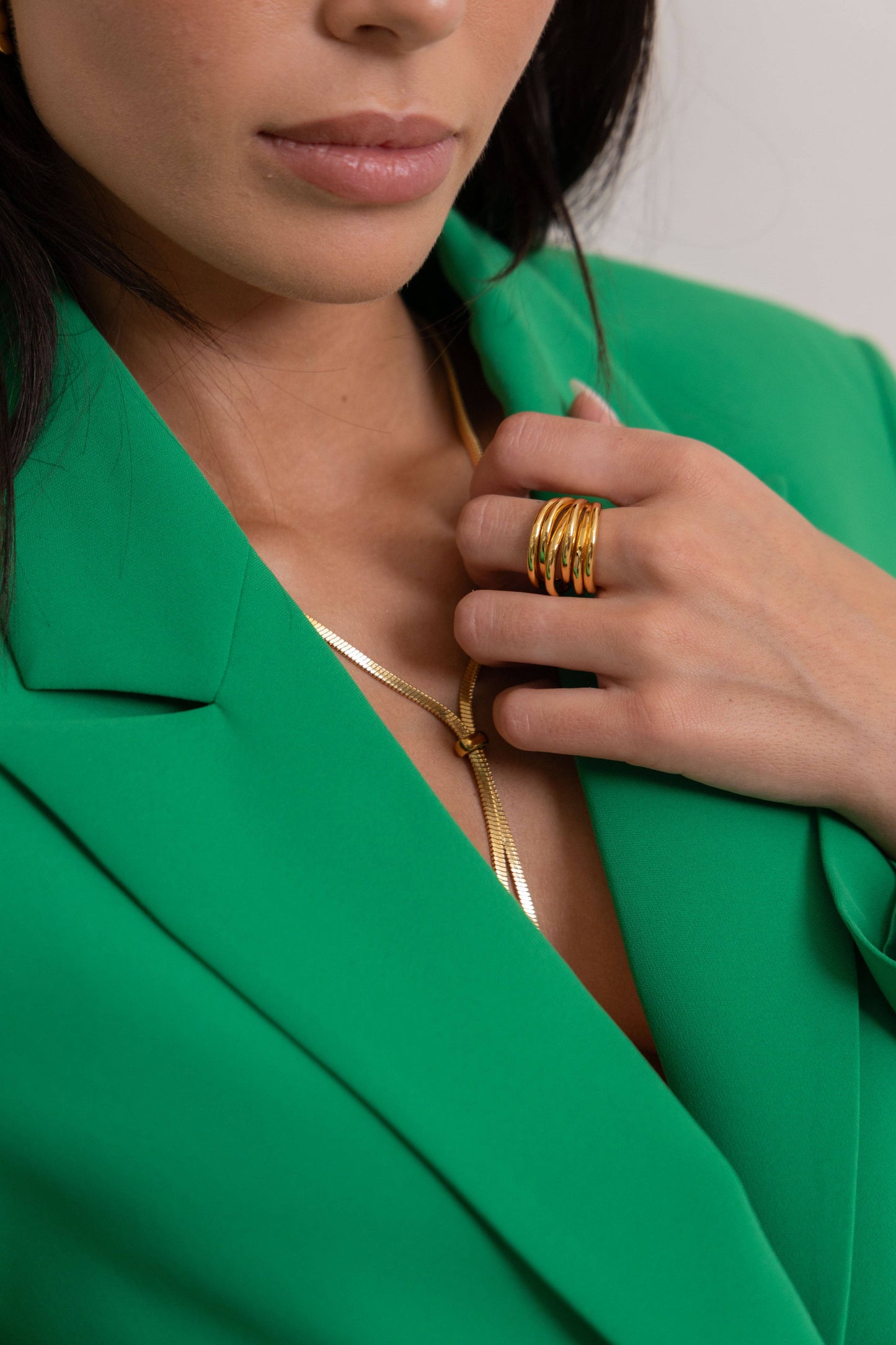 Person wearing a green blazer with gold jewelry and ring.