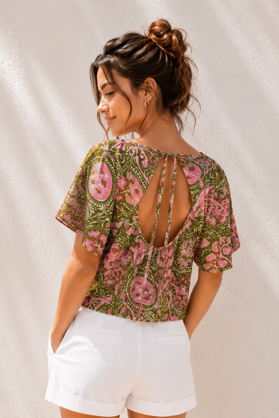 Woman wearing a floral blouse with cut-out design on a neutral background
