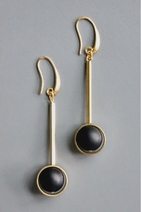Gold earrings with black round stones on a gray background