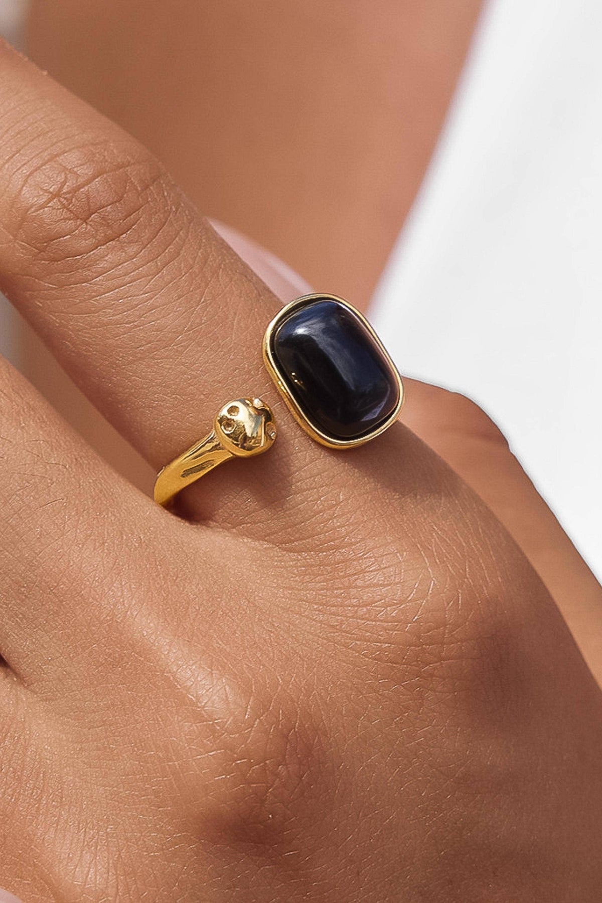 A close-up of a gold ring with a dark oval cabochon stone worn on a person's finger.