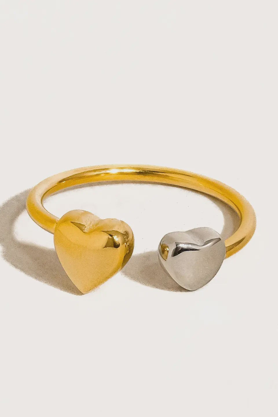 Gold and silver heart-shaped ring on a light gray background