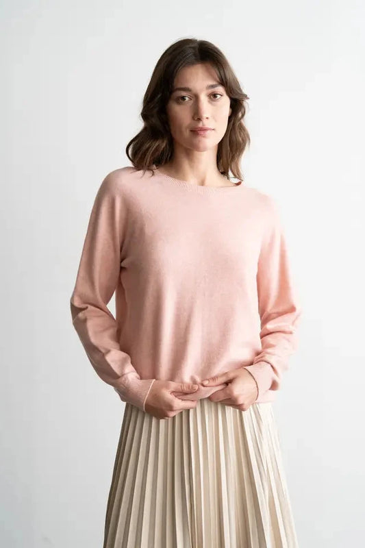 Woman wearing a pink sweater and beige pleated skirt against a white background