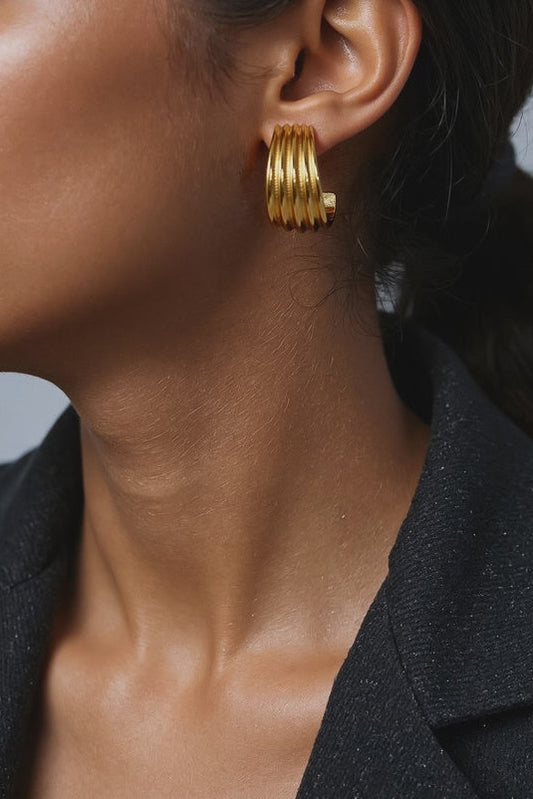 Close-up of a person wearing gold hoop earrings with a blurred background
