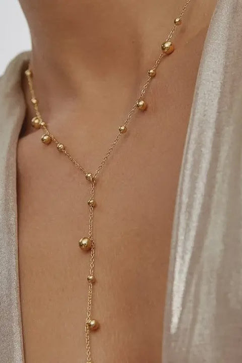 Gold necklace with small beads on a person wearing a light-colored top.