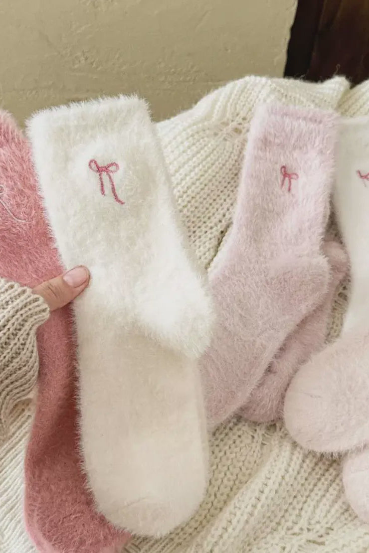 Set of pink and white baby socks with embroidered bows on a textured surface.