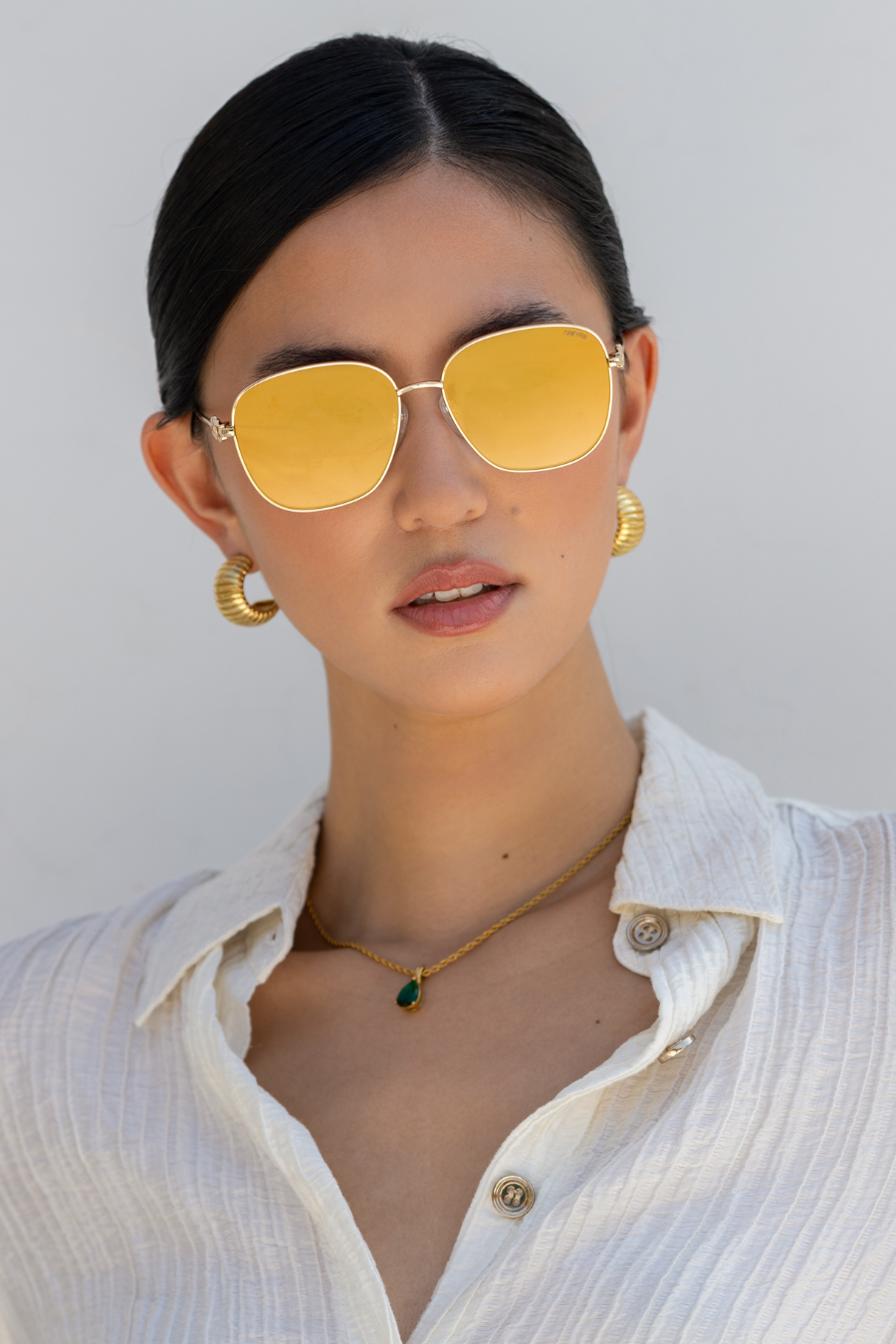 Woman wearing yellow sunglasses and a white shirt against a light background