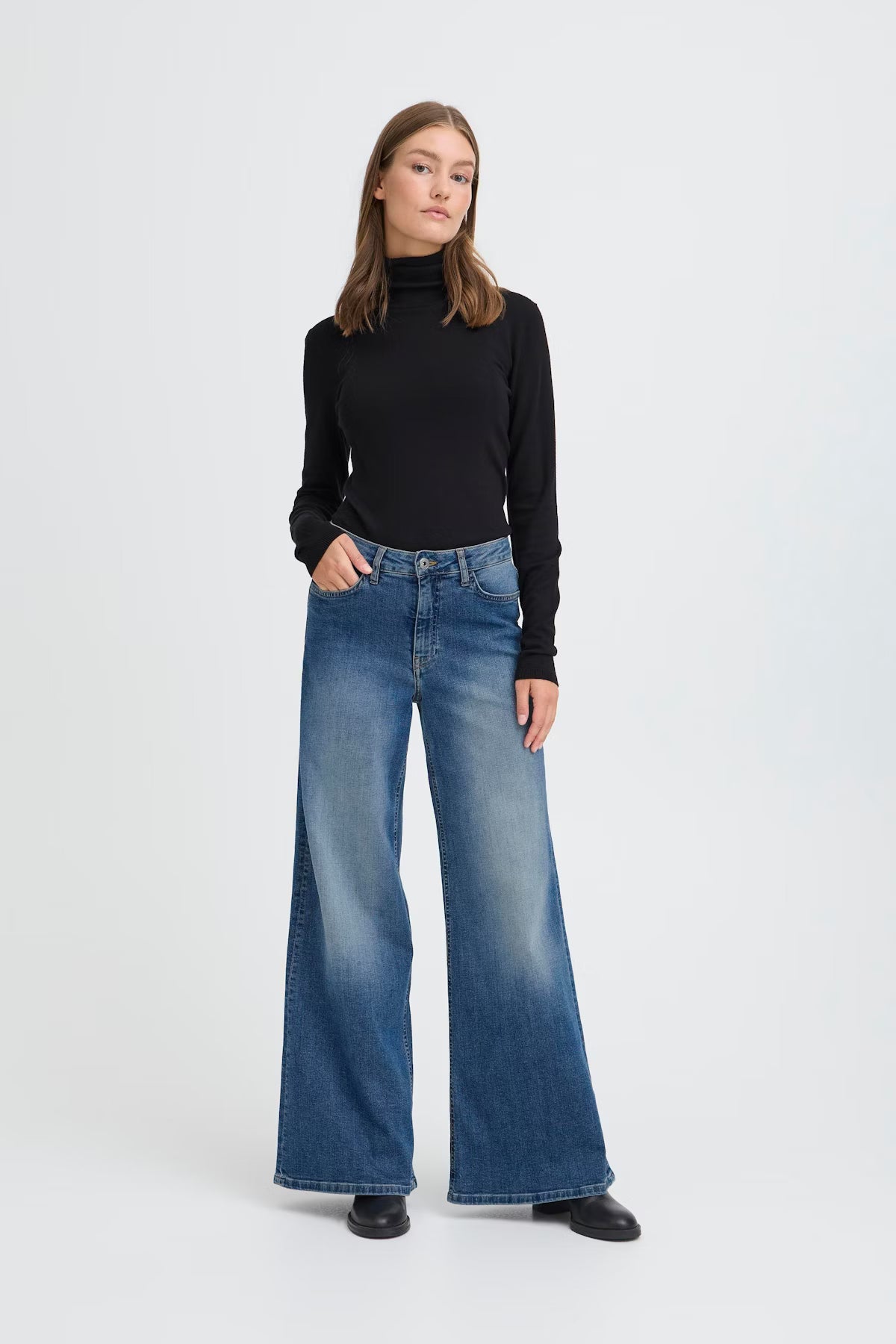 Woman wearing a black turtleneck and blue jeans on a white background