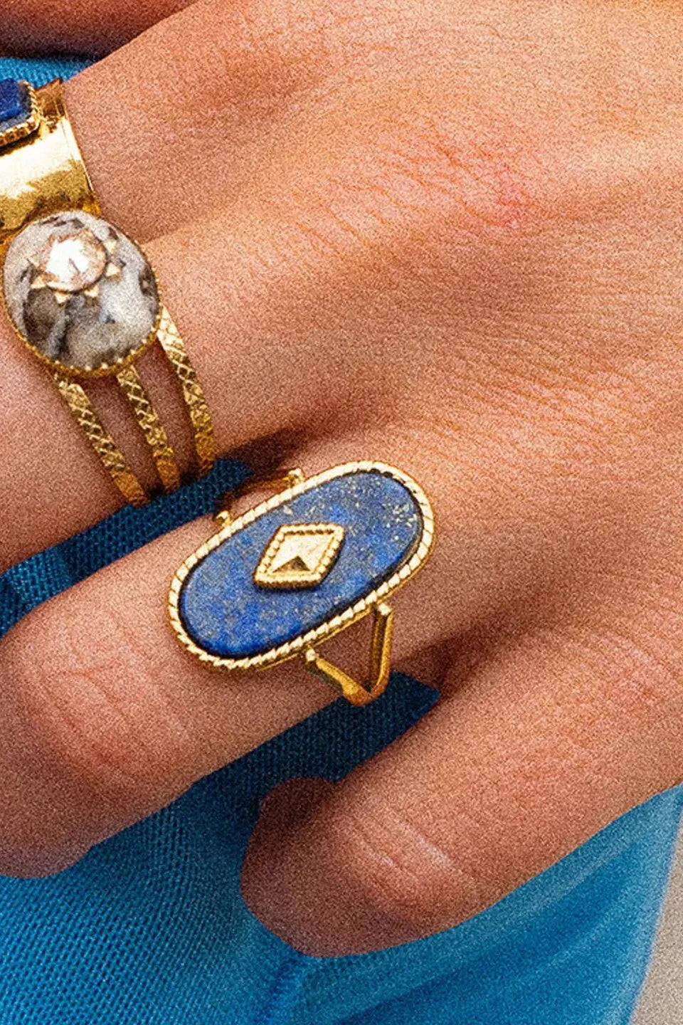 Close-up of a hand wearing multiple rings with blue and gold designs.