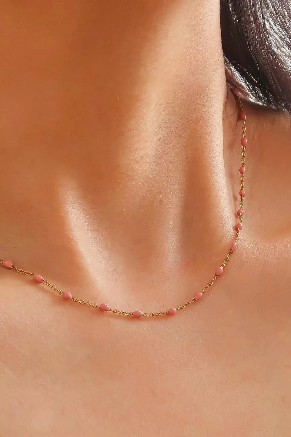 Necklace with pink beads worn by a person, focusing on the necklace and skin texture.