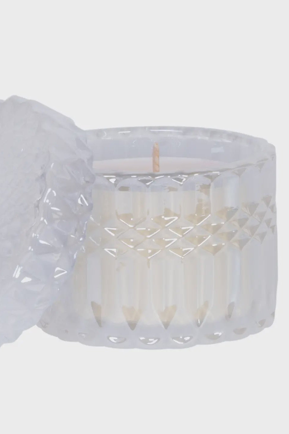 White candle in a textured glass holder with a matching cover on a light gray background