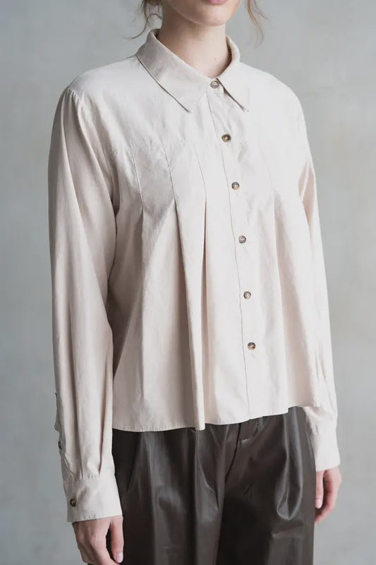 Person wearing a beige button-up shirt and dark pants against a plain background