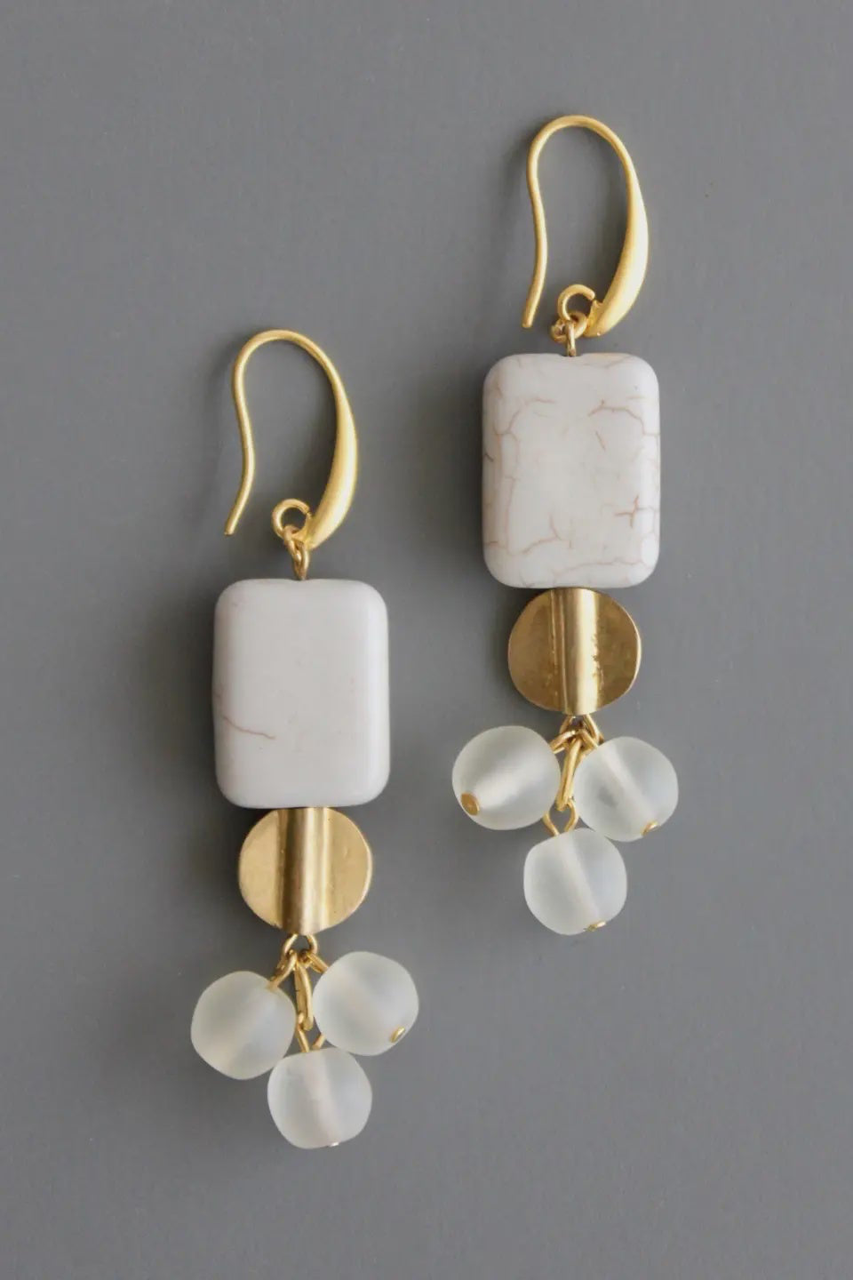 Gold and white stone earrings on a gray background
