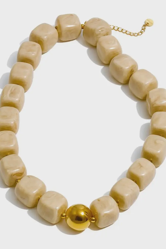 Beige beaded necklace with a gold ball on a white background