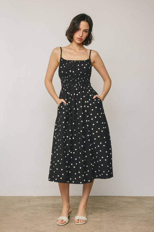 Woman wearing a black dress with white polka dots against a plain background