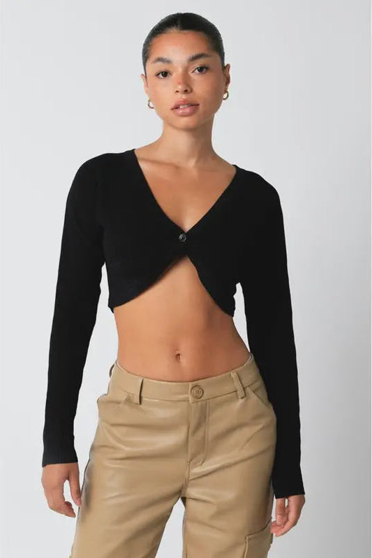 Person wearing a black long-sleeve crop top and beige pants on a white background