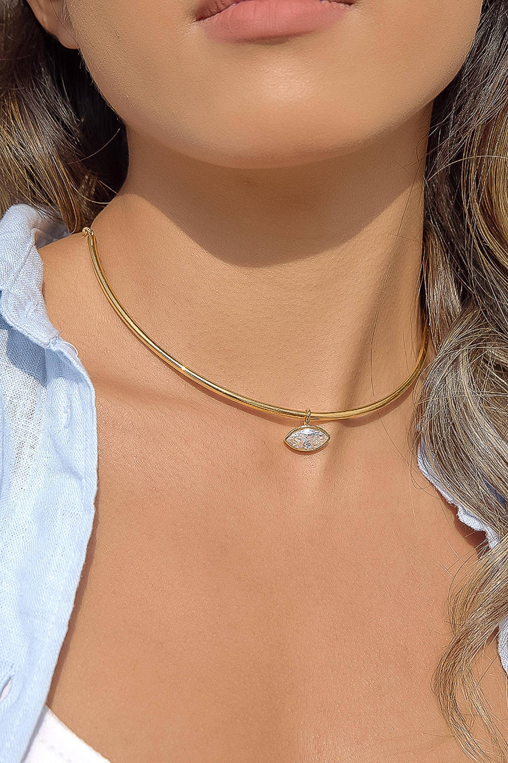 Close-up of a person wearing a gold necklace with a clear stone pendant.