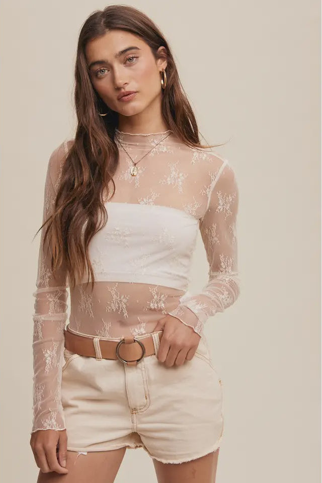 Woman wearing a white lace top and beige shorts on a plain background